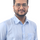 Close-up portrait of a male team member wearing glasses and a light blue shirt against a plain background
