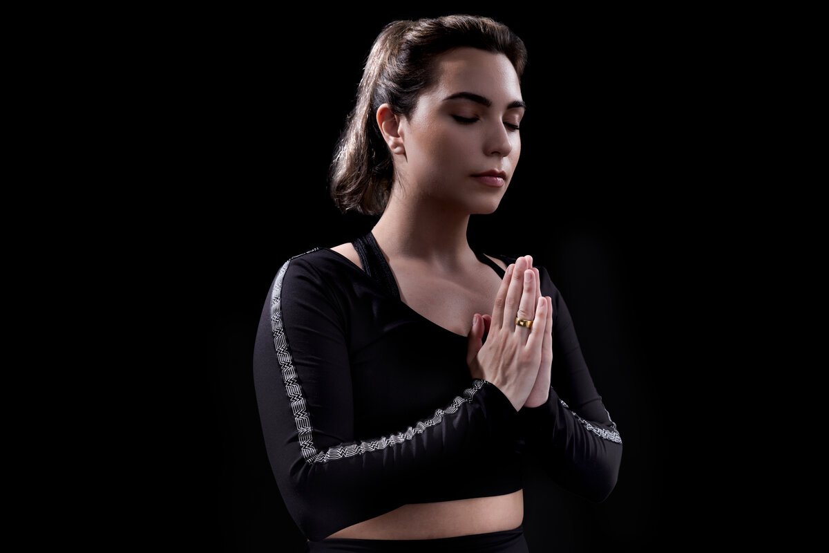 Image showing a person wearing Ultrahuman Ring AIR with hands joined in a pose against a dark background